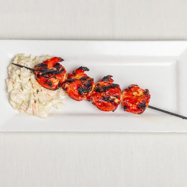 Grilled shrimp skewer with coleslaw on a white rectangular plate.