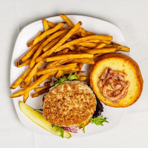 A chicken burger with fries and a pickle spear on a white plate.