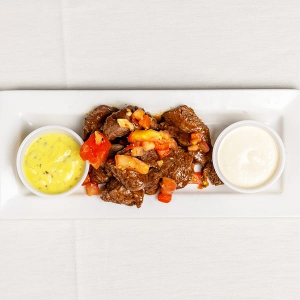 Savory beef stew with diced tomatoes and two dipping sauces on a white rectangular plate.
