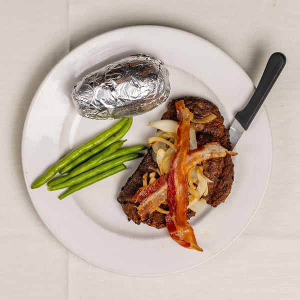 Chopped steak topped with bacon and onions, served with green beans and a foil-wrapped baked potato.