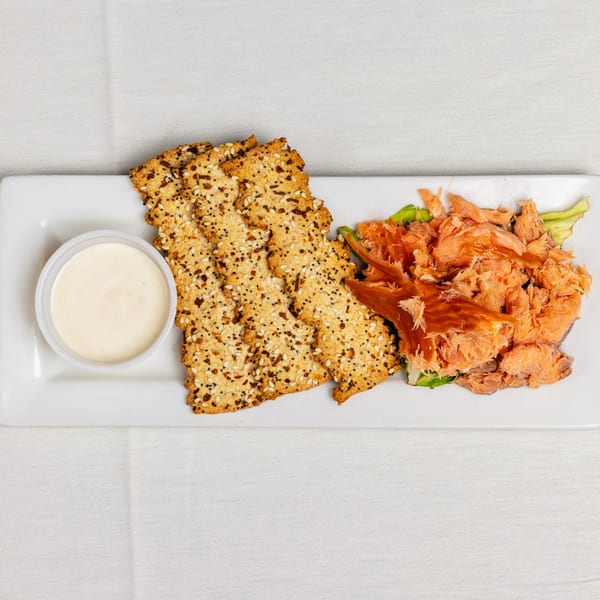 A white rectangular plate with crackers, shredded salmon, and a small cup of sauce.