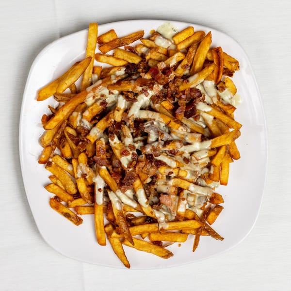Golden french fries topped with creamy white sauce and crispy bacon bits on a white plate.