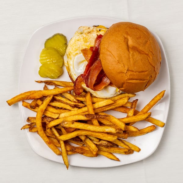 A burger with bacon and a fried egg, served with a side of french fries and pickles.