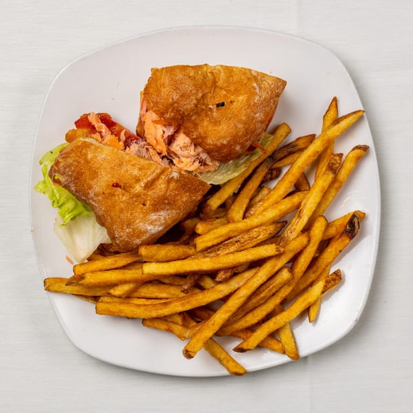 A salmon sandwich on ciabatta bread with lettuce and tomatoes, served with a side of french fries.