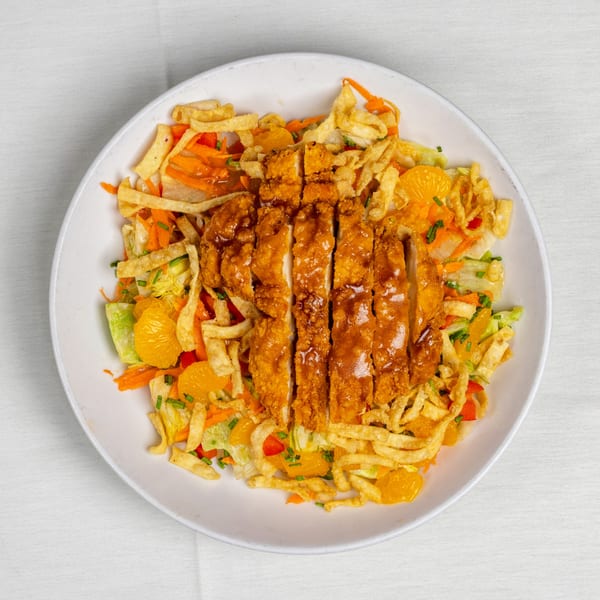 Crispy chicken salad with mandarin oranges, carrots, and fried wonton strips in a white bowl.