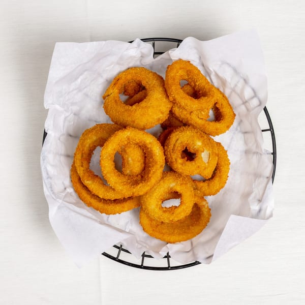 A black wire basket filled with golden-brown, crispy onion rings on white parchment paper.