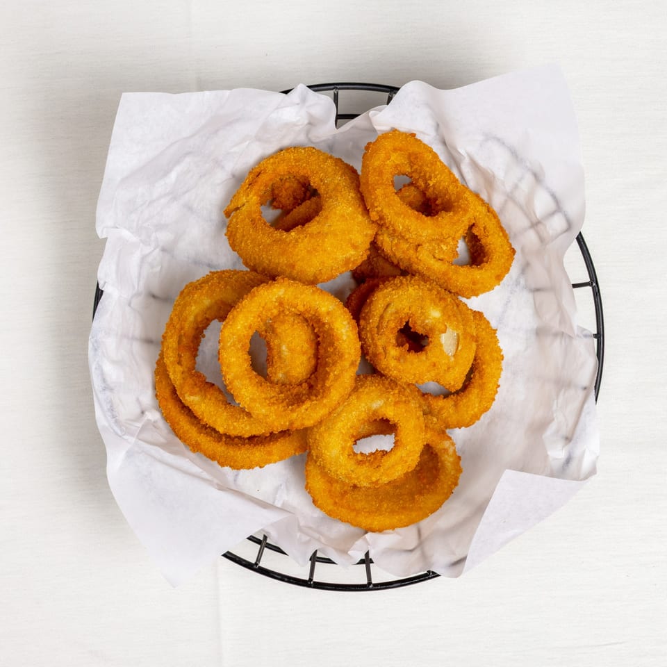 A black wire basket filled with golden-brown, crispy onion rings on white parchment paper.